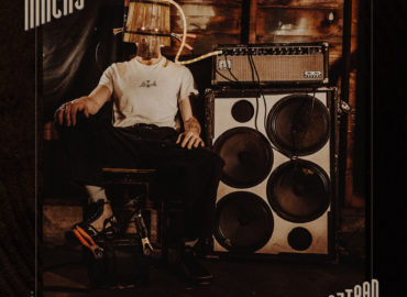 Man sits in chair next to huge amp with a bucket over his head on The Macks album cover for "Dajiban."