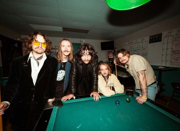Members of The Macks, a Portland rock band, pose around a pool table.