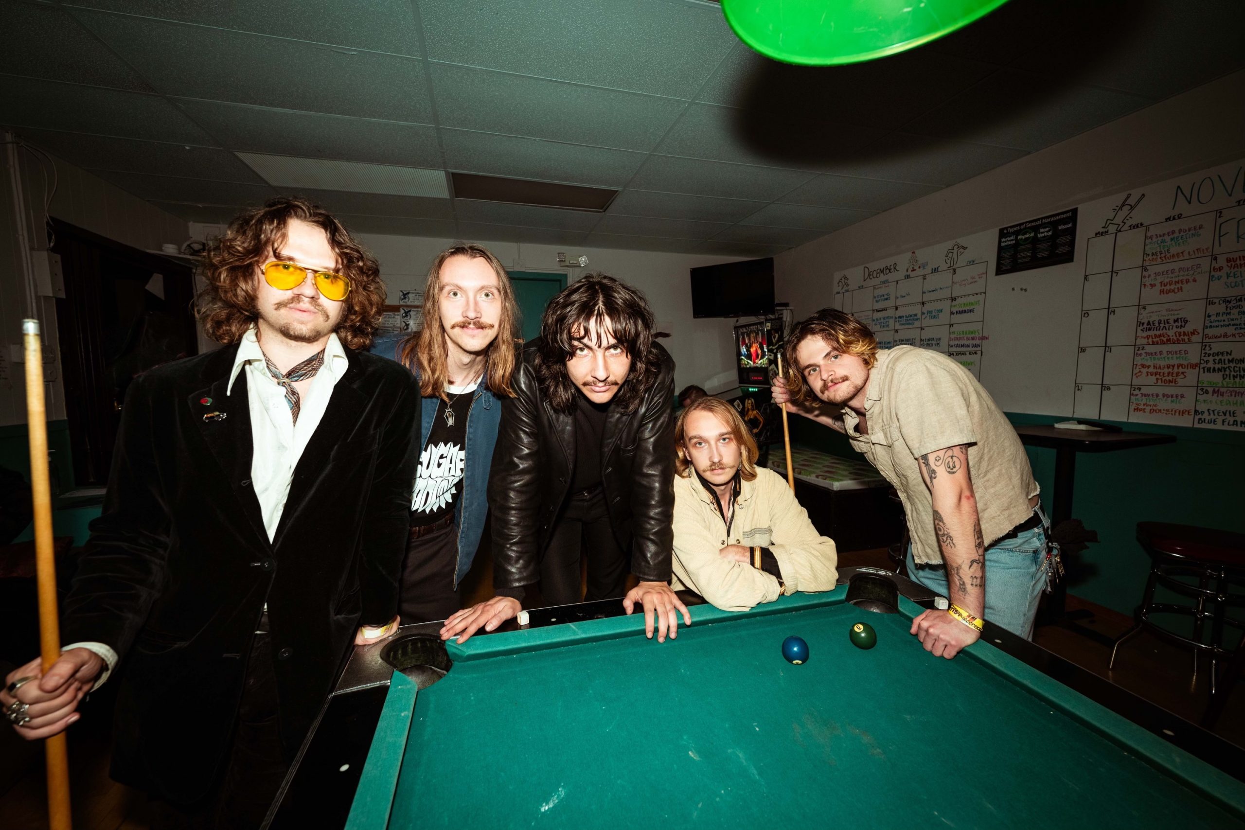 Members of The Macks, a Portland rock band, pose around a pool table.